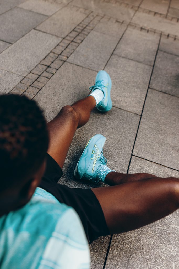 Coureur assis par terre avec des chaussures bleues ascics.